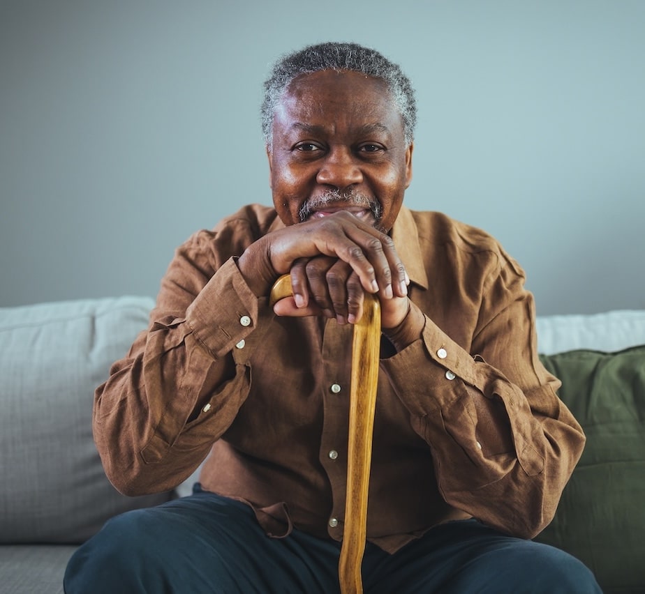 Older man sitting with his hands on a cane and miling